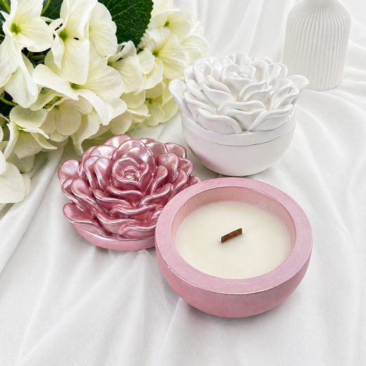 Handgemachte Sojawachskerze in rosa Keramikschale mit Deckel in Kamelienform und Holzdocht, daneben eine weiße Kerzen-Dose vor hellem Hintergrund.