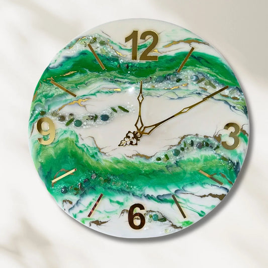 Eine runde Wanduhr aus Epoxidharz im Geoden-Stil mit grünen, weißen und goldenen Mustern, goldenen Zeigern, erhabenen goldenen Ziffern (12, 3, 6, 9) und Strichindizes sowie eingebetteten Dekosteinen und Glitzerelementen vor einem hellen Hintergrund.