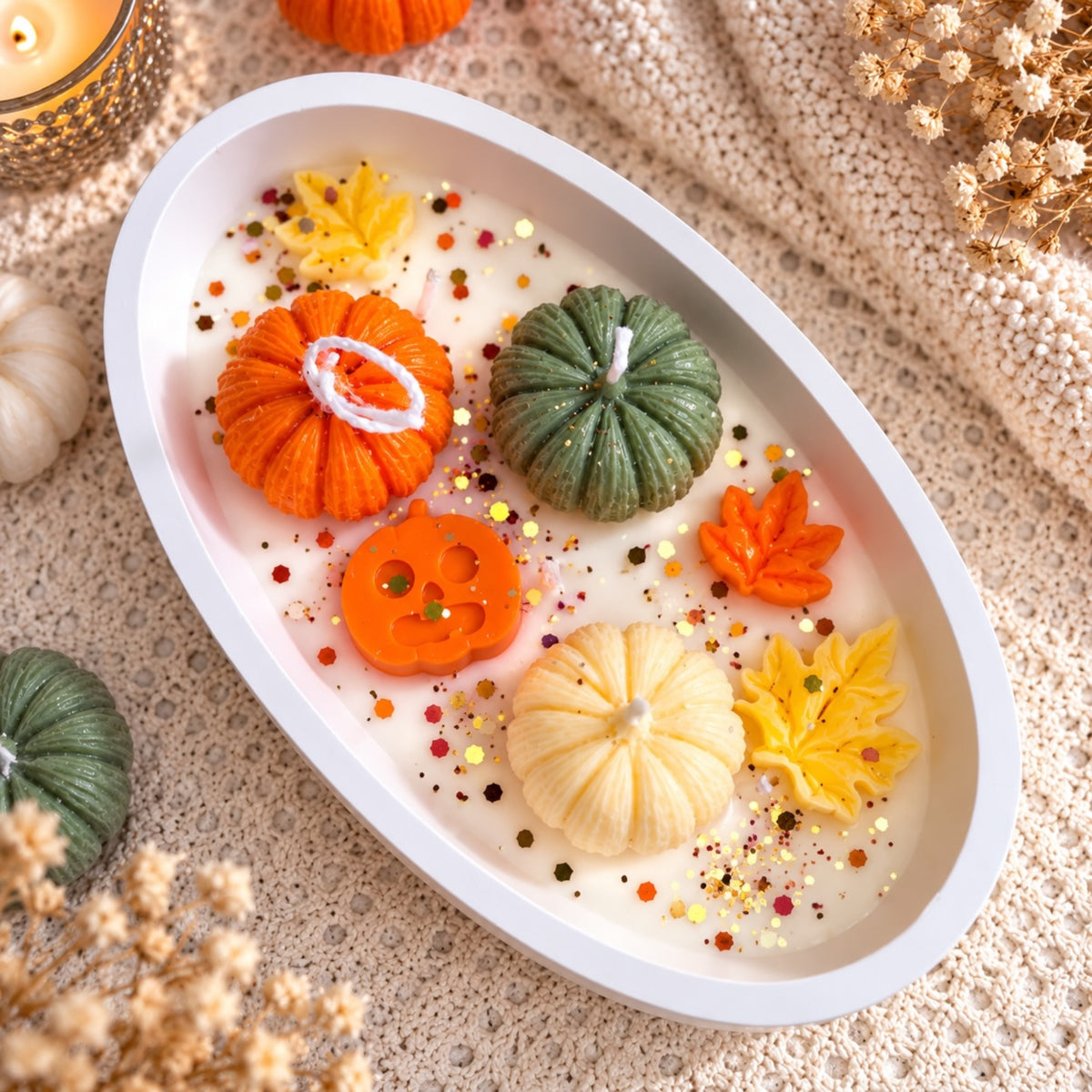 Ovale Kürbis Bowl von oben – orange und grüne Kürbiskerzen mit Herbstblättern und Glitzer in weißer Keramikschale
