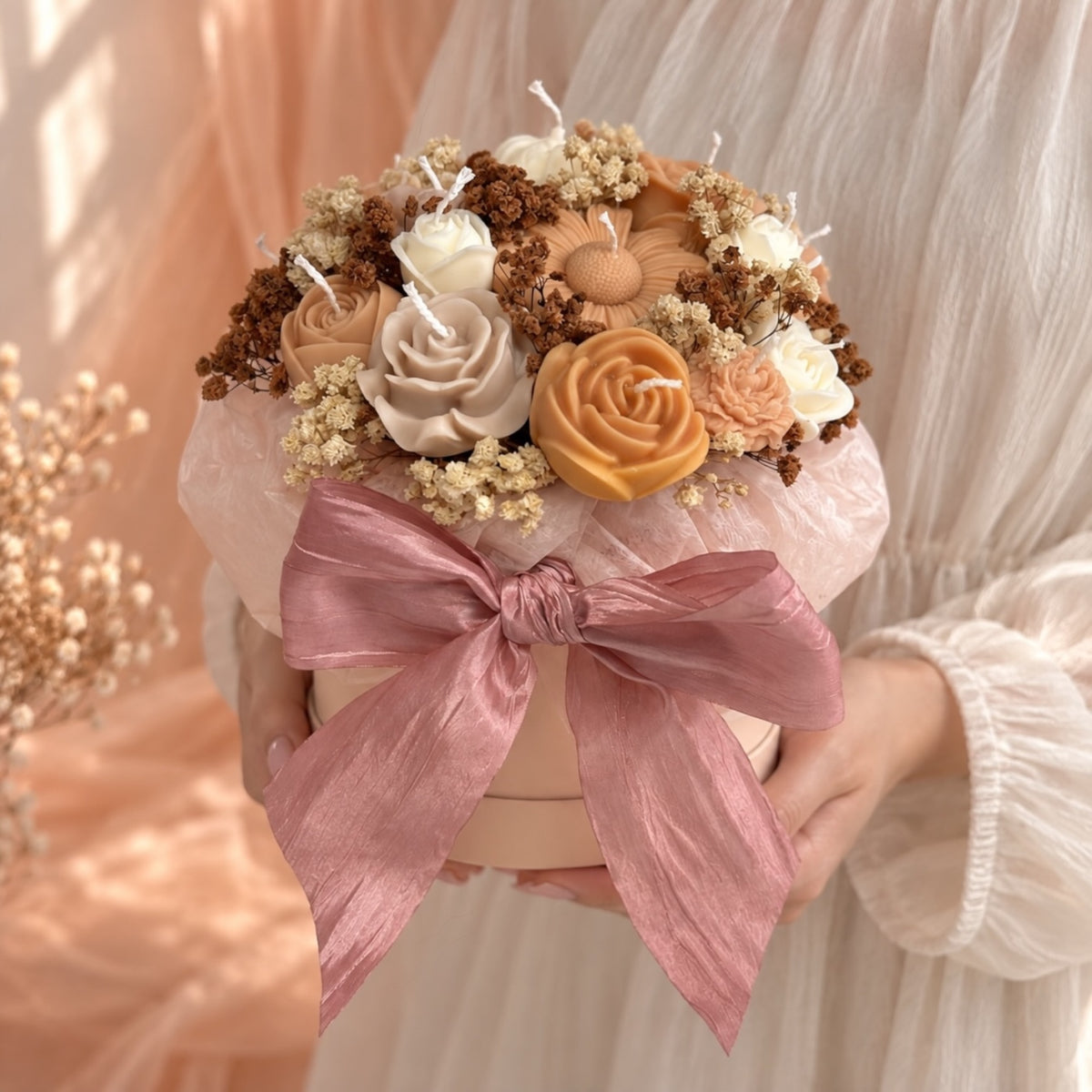 Kerzenblumenstrauß Geschenkbox in den Händen – Rapswachs-Rosen in Beige, Apricot und Orange mit Trockenblumen und rosa Schleife, Geschenkidee Duftkerze von DaarArt


