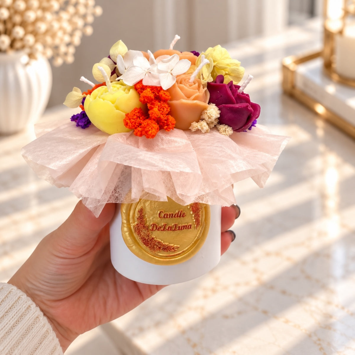 Hand hält ein kleines Kerzenbouquet in weißer Geschenkbox mit Wachsrosen und Trockenblumen
