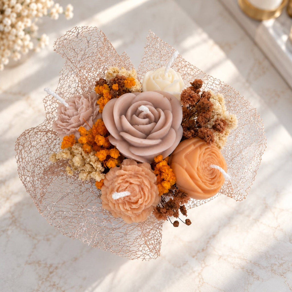 Kerzenstrauß von oben mit Rosenkerze in Altrosa, Pfingstrosen in Pfirsich, weißer Rose und orangem Schleierkraut in roségoldenem Netz
