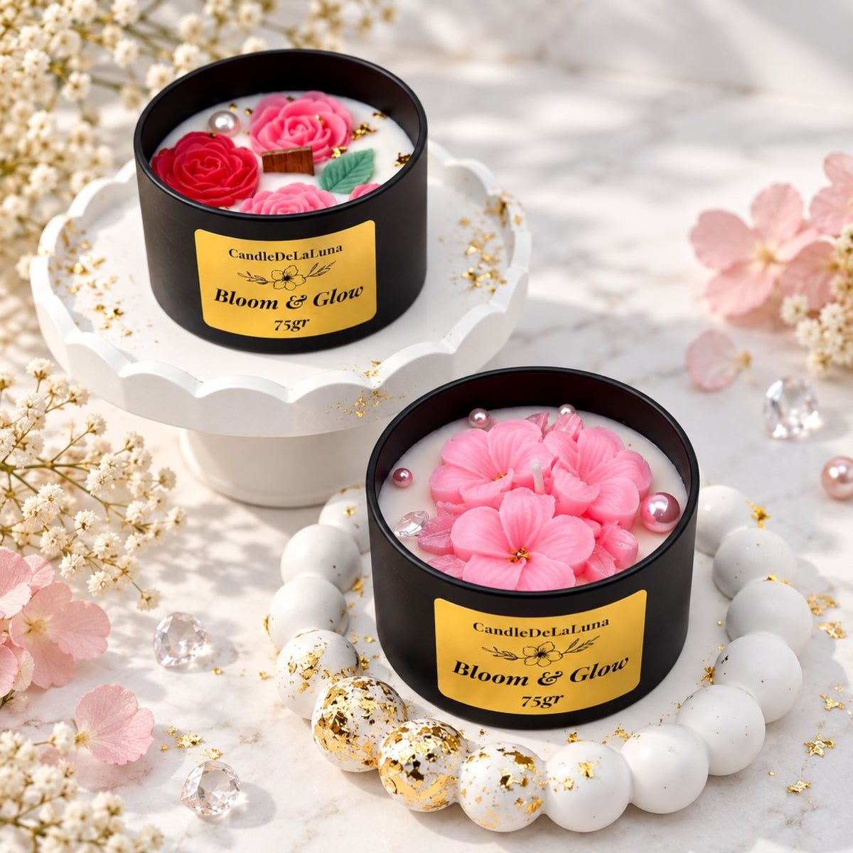 Zwei Blumenkerzen in schwarzen Dosen mit Rosenmotiven und rosa Blüten auf dekorativen Tabletts
