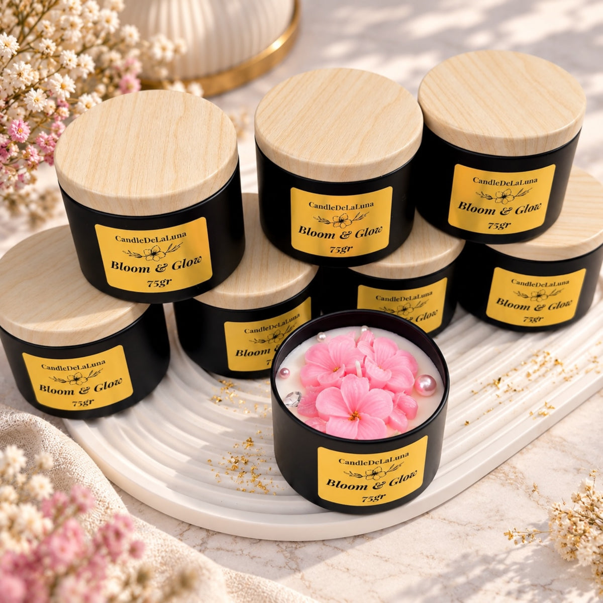 Mehrere schwarze Kerzendosen mit hellen Deckeln und eine offene Kerze mit rosa Blütenmotiv
