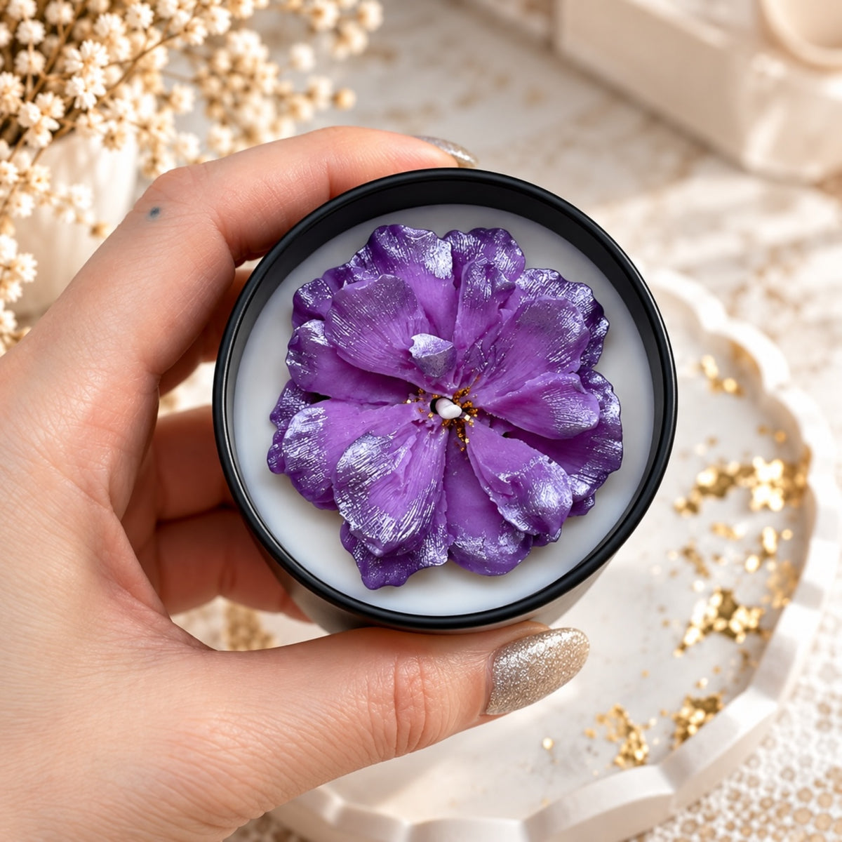 Kerze in schwarzer Dose mit großer violetter Blüte auf weißer Oberfläche, von oben fotografiert
