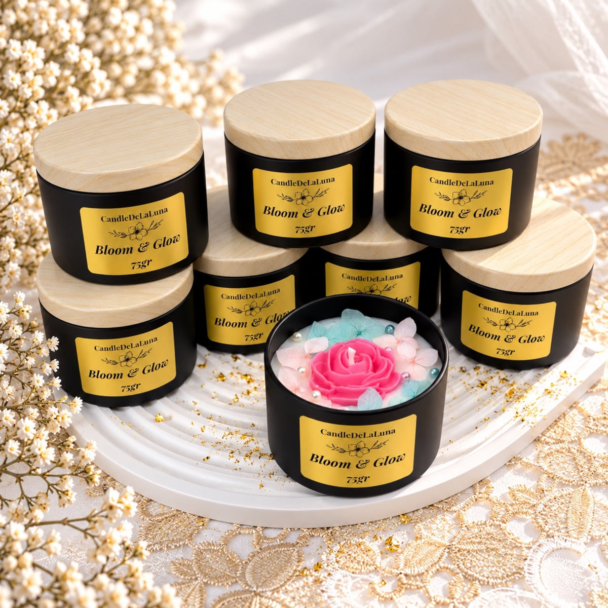 Mehrere geschlossene schwarze Kerzendosen mit hellen Deckeln und eine offene Blumenkerze mit pinkem Rosenmotiv
