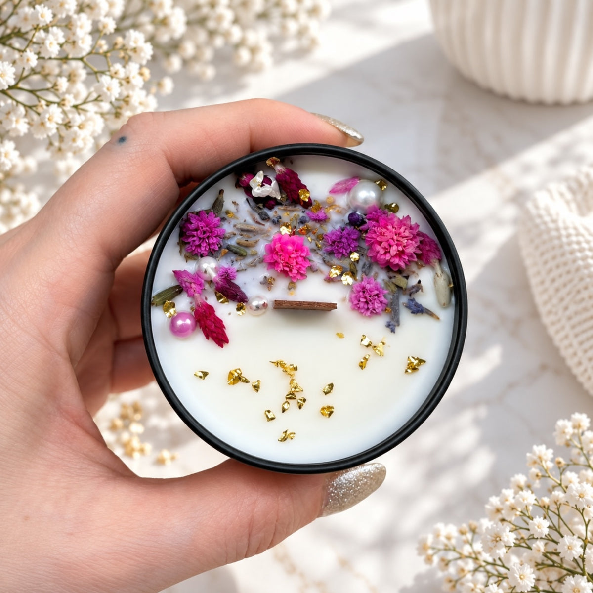 Blumenkerze mit kleinen pinken Blüten, getrockneten Blütenteilen und goldfarbenen Akzenten in schwarzer Dose
