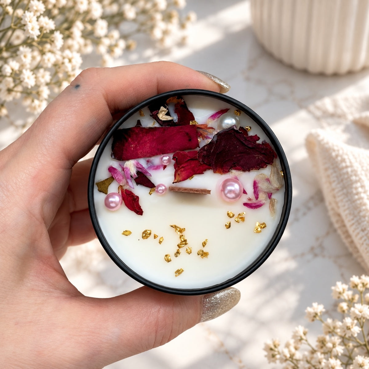 Blumenkerze in schwarzer Dose mit roten Rosenblättern, rosa Perlen und goldfarbenen Akzenten, von oben fotografiert
