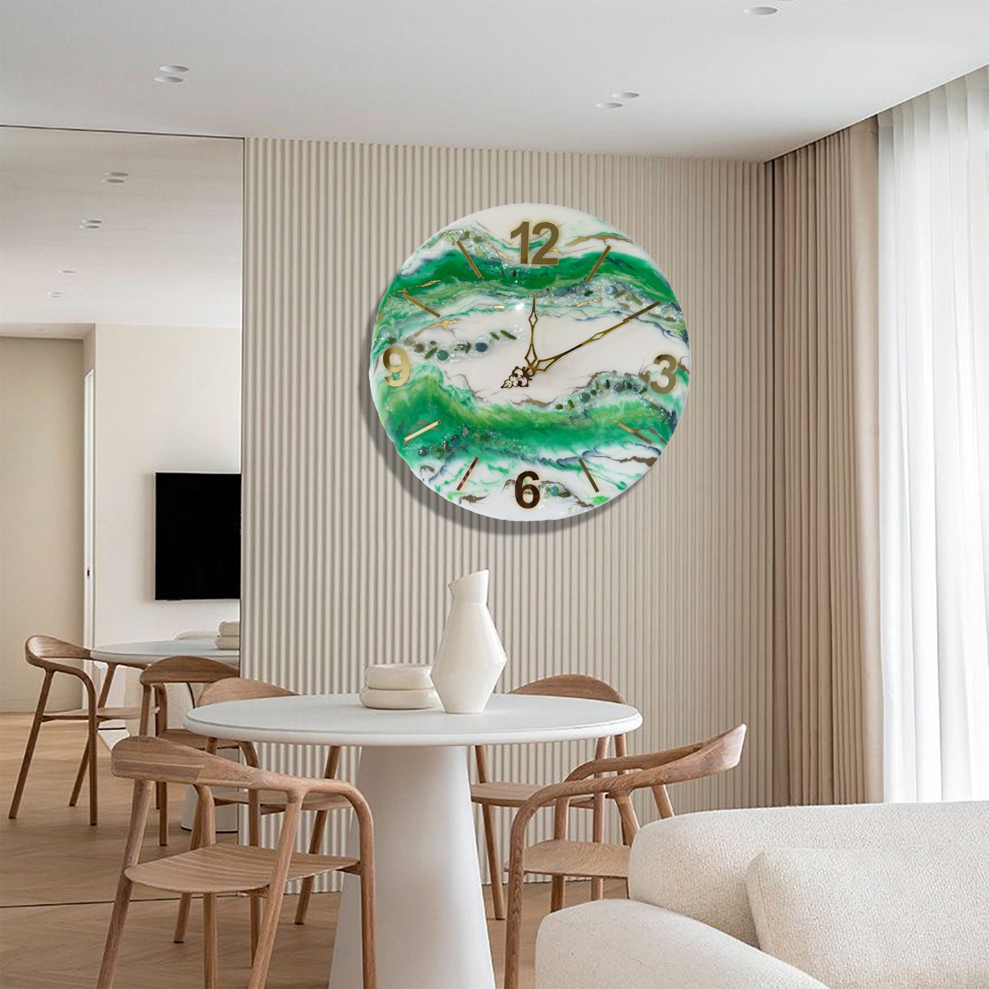 Eine runde Wanduhr aus Epoxidharz im Geoden-Stil mit grünen, weißen und goldenen Mustern, aufgehängt an einer hellen Wand mit vertikaler Rillenstruktur in einem modernen Esszimmer über einem runden weißen Tisch mit Holzstühlen.