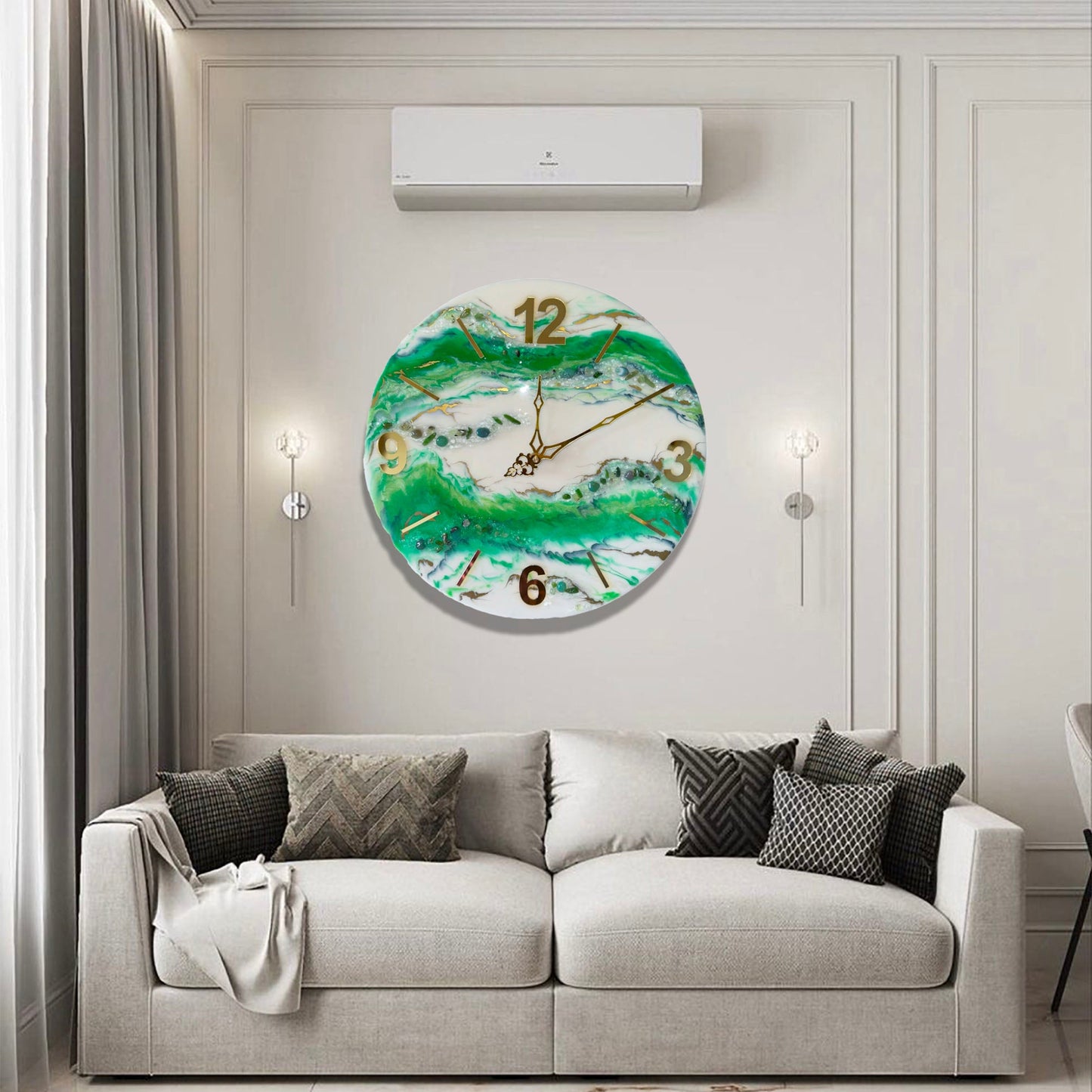 Eine runde Wanduhr aus Epoxidharz im Geoden-Stil mit grünen, weißen und goldenen Mustern, aufgehängt an einer hellen Wand mit Zierleisten über einem grauen Sofa mit Kissen, flankiert von zwei minimalistischen Wandleuchten unter einer Klimaanlage.