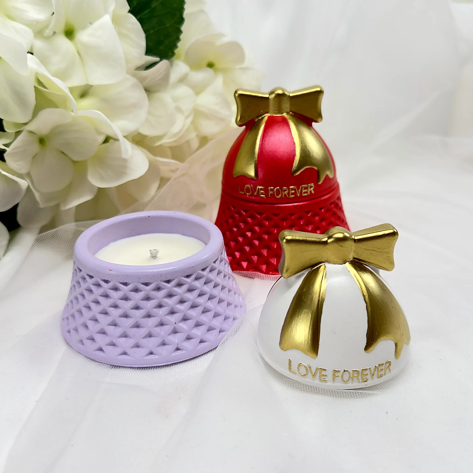Nahaufnahme von „Love Forever“ Kerzen in Rot und Lavendel mit goldenen Schleifen-Deckeln, eine Kerze geöffnet auf weißem Tüllhintergrund.