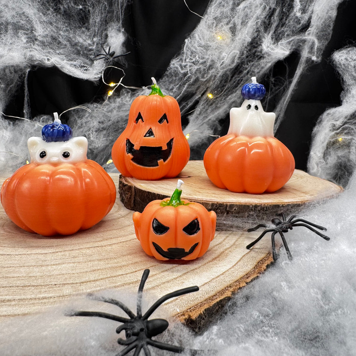 Kürbis Halloween Kerzen: Katze und Gespenst auf Kürbis mit blauen Mini-Kürbissen und zwei Jack O’Lantern Kerzen auf Holzscheibe
