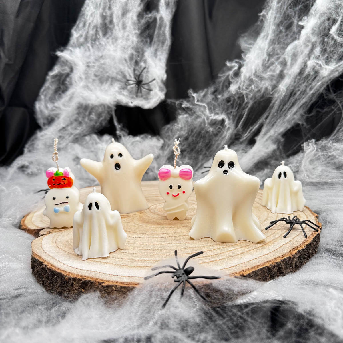 Sechs verschiedene Geisterkerzen in Weiß auf Holzscheibe als Halloween Tischdeko mit Spinnennetz
