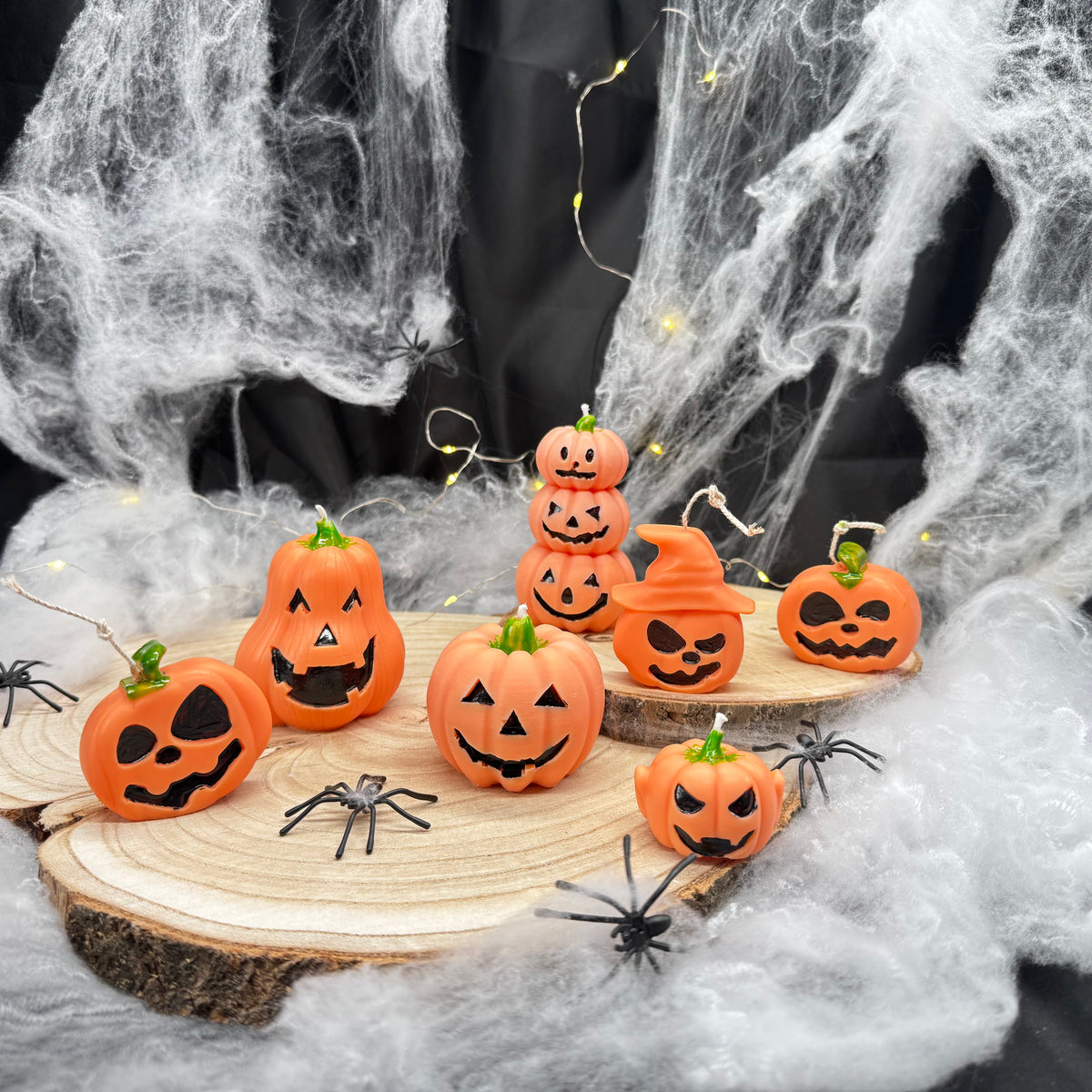 Sieben orangefarbene Halloween-Kürbiskerzen mit unterschiedlichen Gesichtern auf Holzscheiben
