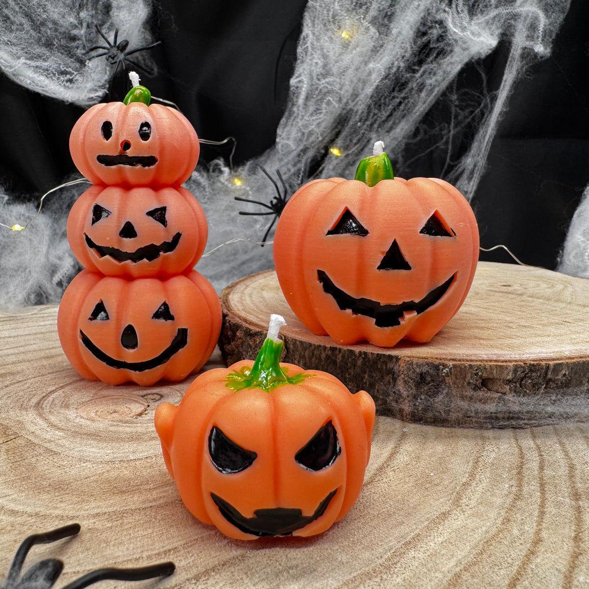 Drei Kürbiskerzen mit verschiedenen Jack-O’-Lantern-Gesichtern auf Holzscheiben
