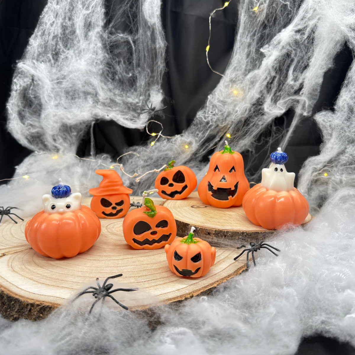 Acht verschiedene Kürbiskerzen mit Jack O’Lantern Gesichtern, Hexenhut, Katze und Gespenst auf Holzscheiben mit Spinnweben
