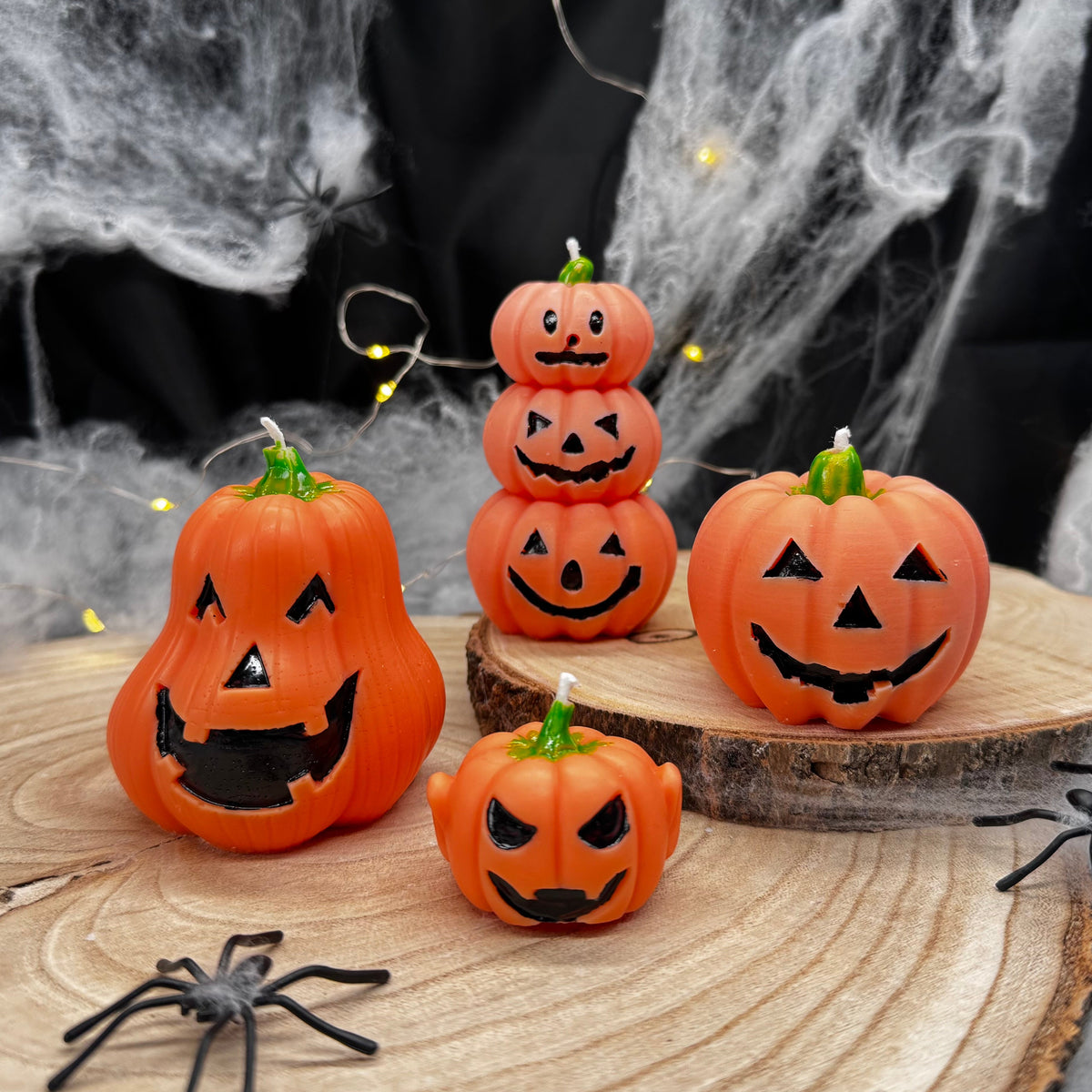 Orangefarbene Kürbiskerzen mit verschiedenen Gesichtern auf Holzscheiben vor Halloween-Dekoration
