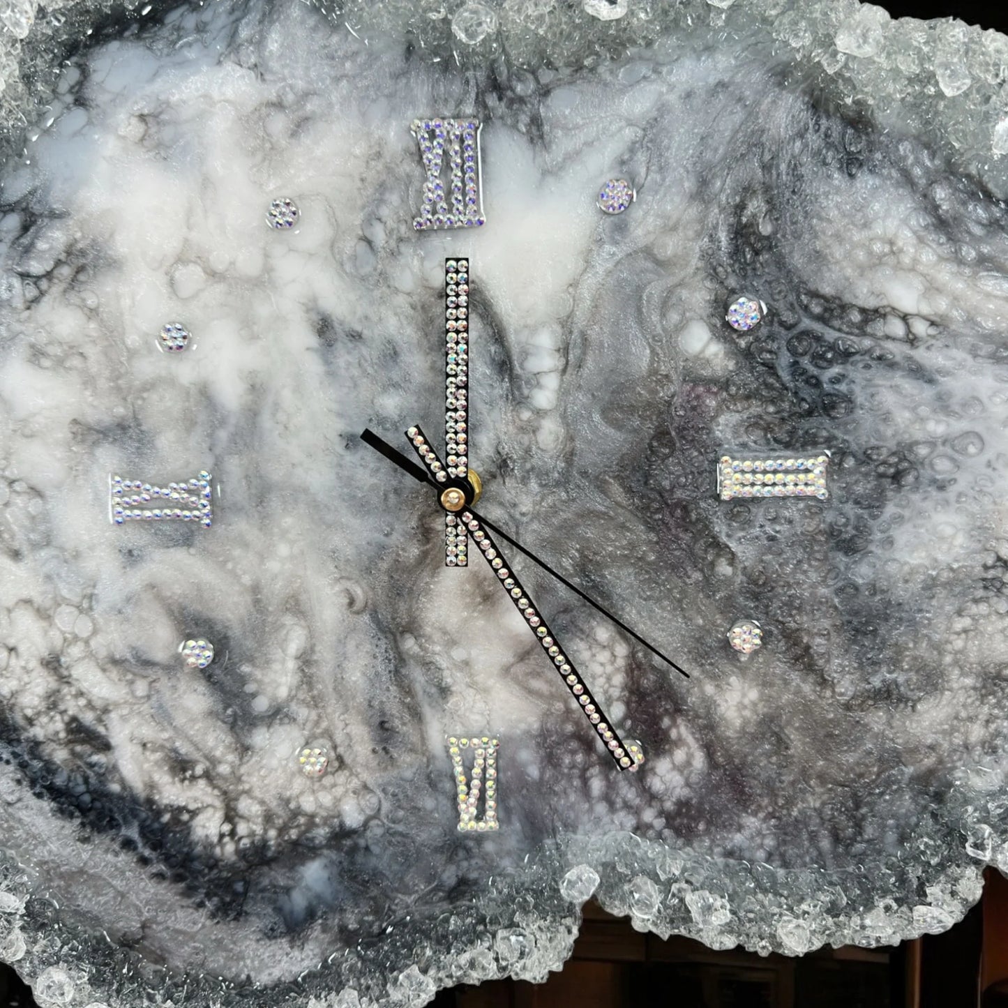 Nahaufnahme einer handgefertigten Wanduhr aus Epoxidharz mit Marmormuster, verzierten Zeigern und römischen Ziffern aus glitzernden Strasssteinen