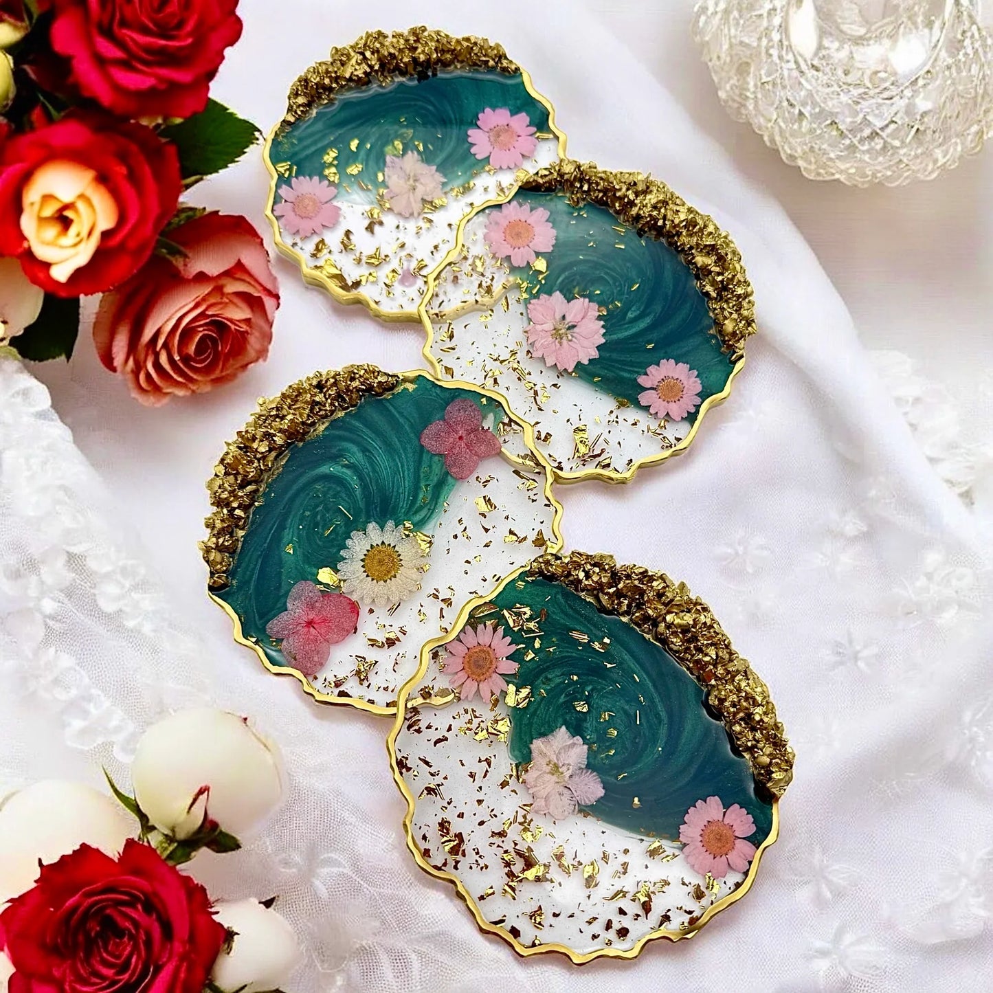 Draufsicht auf ein 4er Set handgefertigter Untersetzer aus Resin mit echten rosa Blüten und Goldakzenten, dekoriert mit frischen Rosen auf weißer Spitze.
