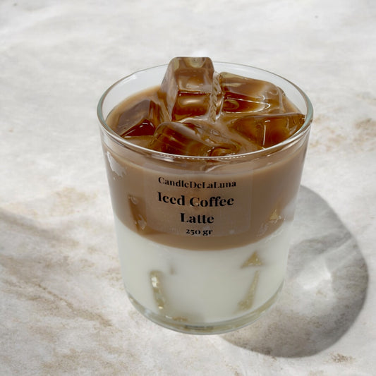 Eine dekorative Kerze im Glas, gestaltet wie ein Eiskaffee-Latte mit einer weißen Schicht unten, einer hellbraunen Kaffeeschicht oben und realistisch wirkenden Wachs-Eiswürfeln an der Oberfläche.