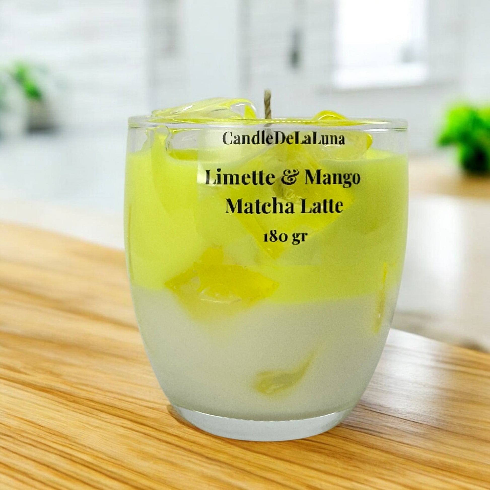 Eine dekorative Kerze im Glas, gestaltet wie ein Limette & Mango Matcha Latte mit einer weißen Schicht unten, einer hellgelben Schicht oben und transparenten Wachs-Eiswürfeln an der Oberfläche.