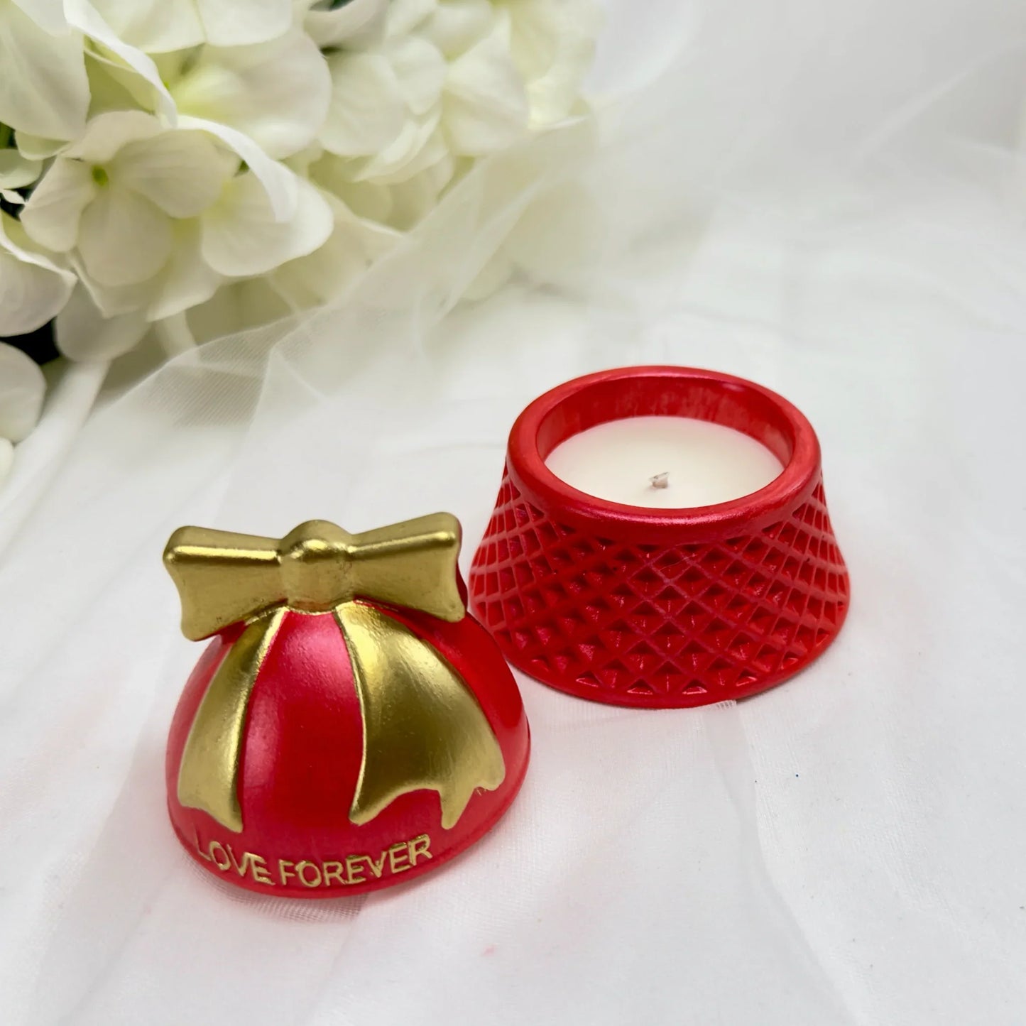 Rote Sojawachskerze in einer strukturierten Keramikdose mit goldenem Schleifen-Deckel und der Aufschrift „Love Forever“ neben weißen Blumen.