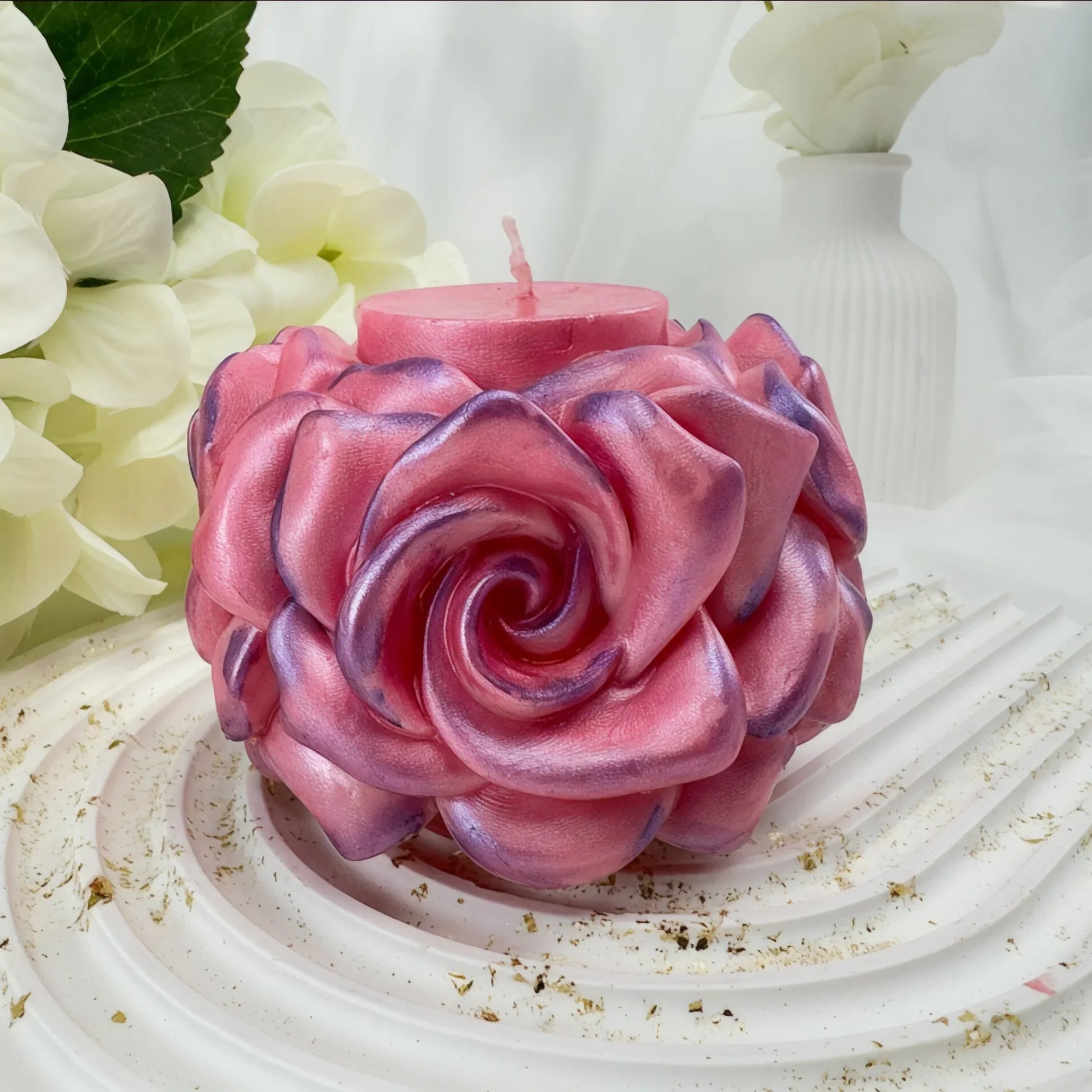 Nahaufnahme einer handgefertigten rosa Rosenkerze mit perlmuttartigem Glanz und violetten Akzenten auf einem weißen Dekotablett.