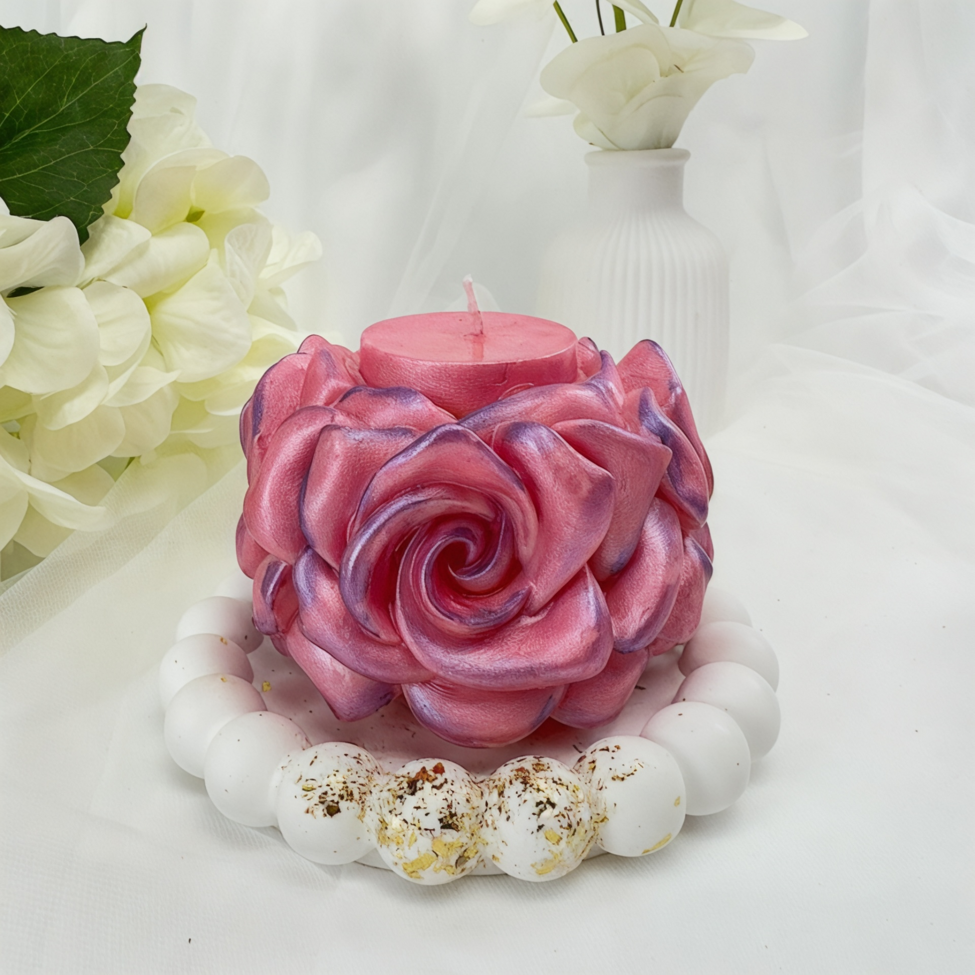 Eine handgefertigte rosa Rosenkerze mit perlmuttartigem Glanz auf einem weißen runden Tablett mit Perlenrand.