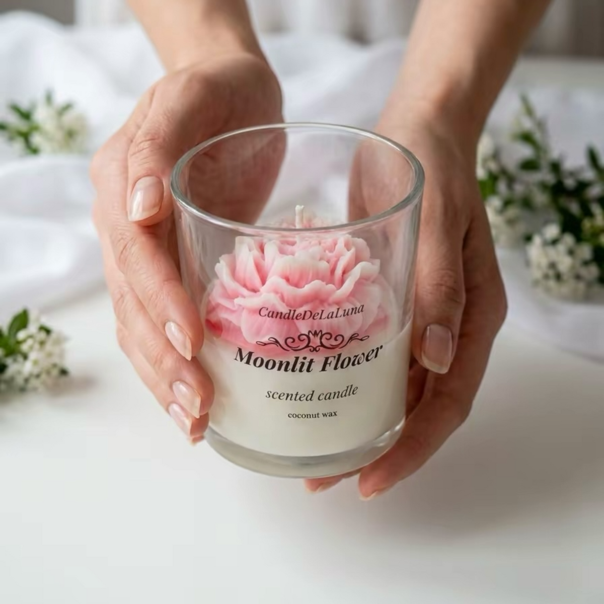 Blumenkerze im Glas mit rosafarbener Pfingstrosenform, von beiden Händen gehalten
