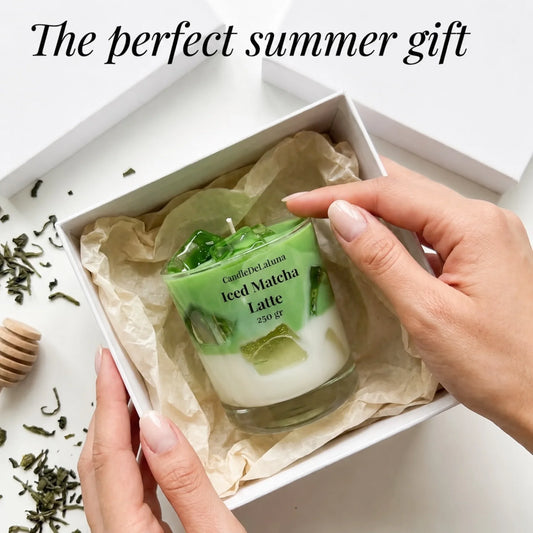 Eine Werbegrafik zeigt Hände, die eine dekorative Kerze in Form eines Iced Matcha Latte aus einer weißen Geschenkschachtel nehmen, ergänzt durch verstreute Teeblätter und den Text „The perfect summer gift“.